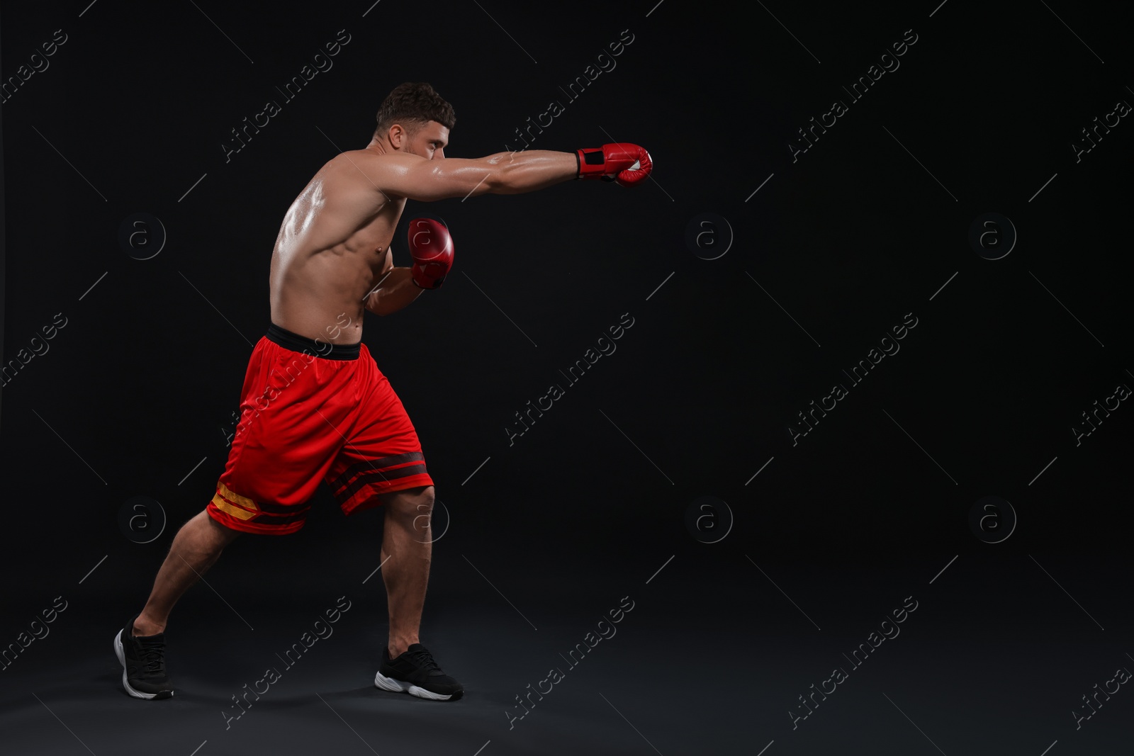 Photo of Man in boxing gloves fighting on black background. Space for text