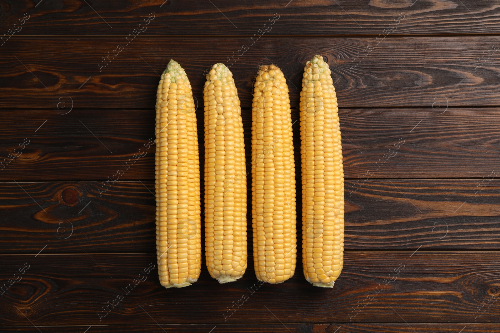 Photo of Tasty sweet corn cobs on wooden table, flat lay