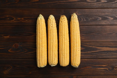 Photo of Tasty sweet corn cobs on wooden table, flat lay