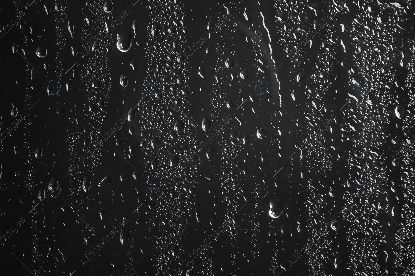 Photo of Glass with rain drops against dark background