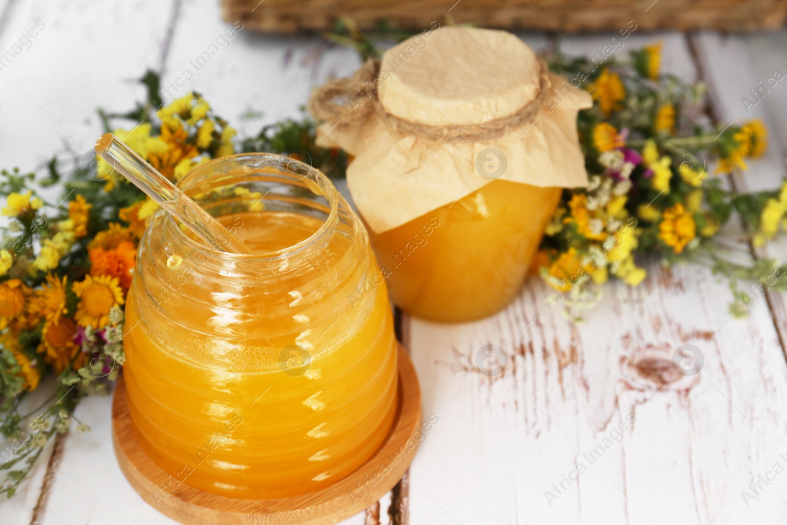 Photo of Delicious fresh honey and beautiful flowers on white wooden table indoors