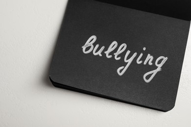 Word Bullying written in black notebook on white stone surface, top view