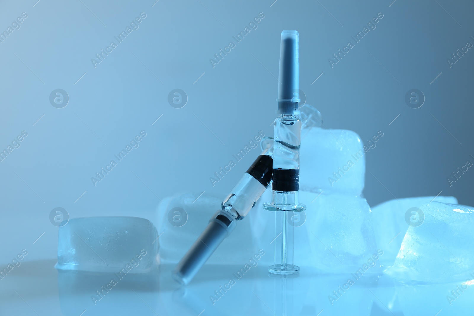 Photo of Syringes with COVID-19 vaccine and ice cubes on white table