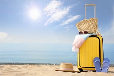 Photo of Yellow suitcase with beach items on sandy seashore, space for text