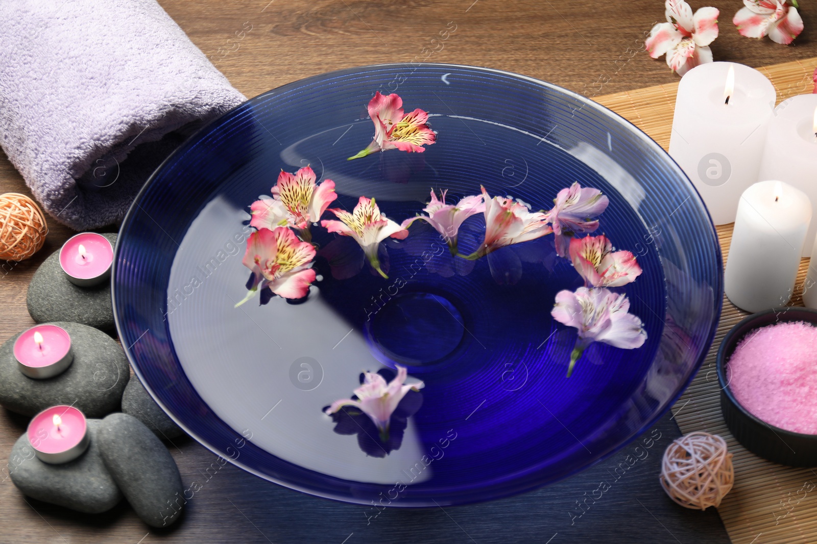 Photo of Bowl of water with flowers and different spa supplies on wooden table