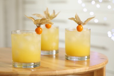 Photo of Refreshing cocktails decorated with physalis fruits on wooden table against blurred festive lights