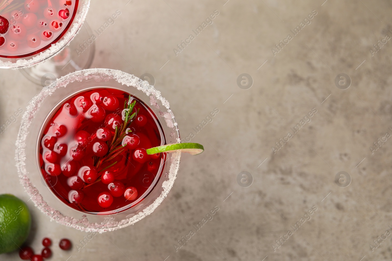 Photo of Tasty cranberry cocktail with rosemary and lime in glasses on grey table, flat lay. Space for text