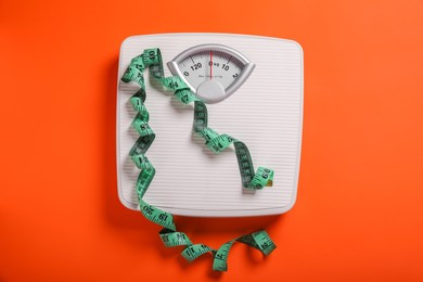 Photo of Scales and measuring tape on orange background, top view. Weight loss concept