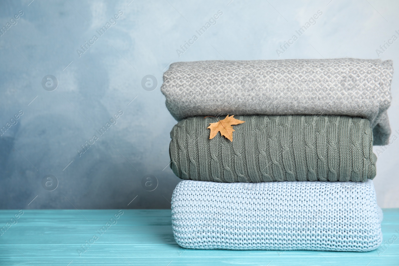 Photo of Stack of soft plaids and dry leaf on light blue wooden table. Space for text