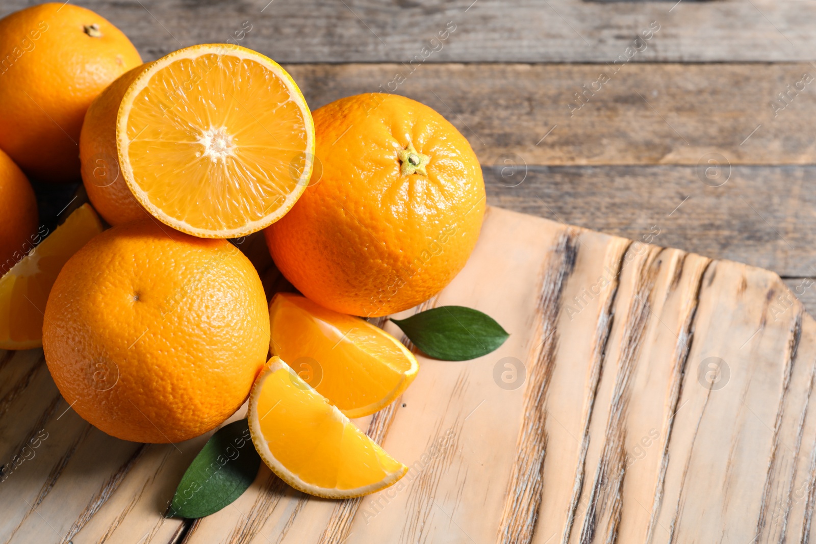 Photo of Fresh oranges with leaves on wooden table, space for text