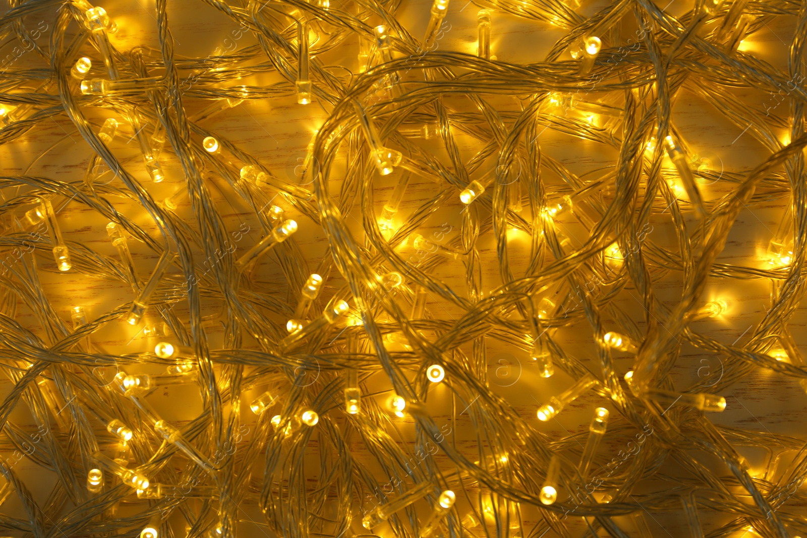 Photo of Glowing Christmas lights on white wooden background, top view