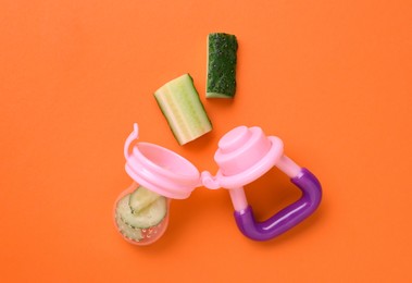 Photo of Nibbler with fresh cucumber on orange background, flat lay. Baby feeder