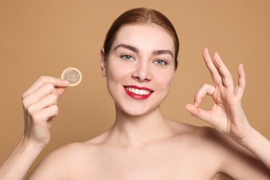 Photo of Woman with condom showing ok gesture on beige background. Safe sex