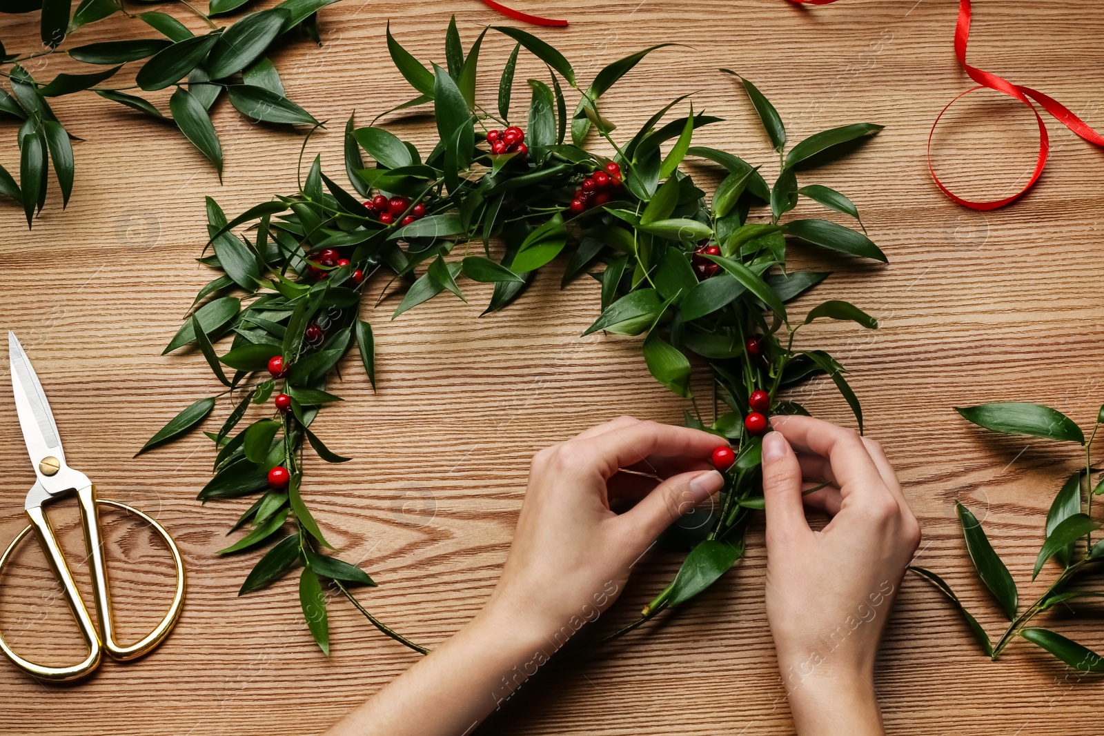 Photo of Florist making beautiful mistletoe wreath at wooden table, top view. Traditional Christmas decor