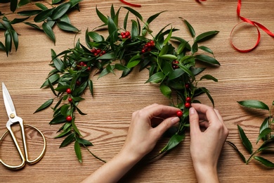 Florist making beautiful mistletoe wreath at wooden table, top view. Traditional Christmas decor