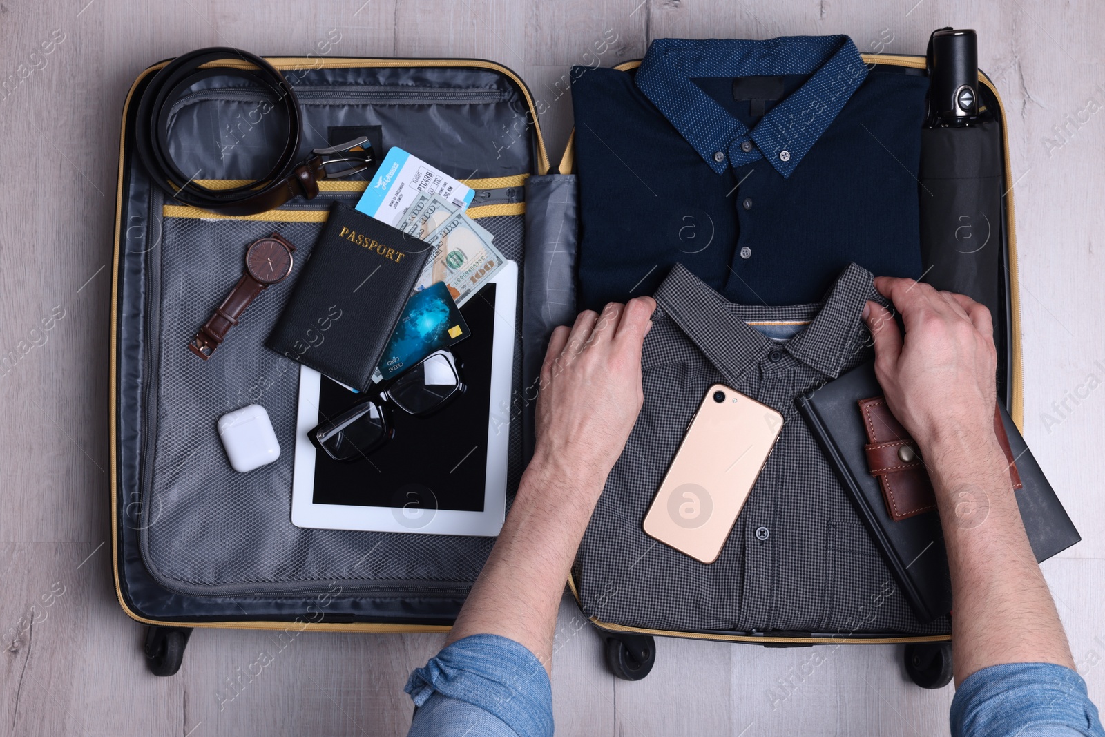 Photo of Man packing suitcase for business trip on wooden floor, top view