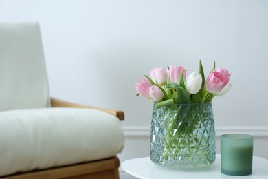 Vase with beautiful tulips and candle on table indoors, space for text. Interior elements