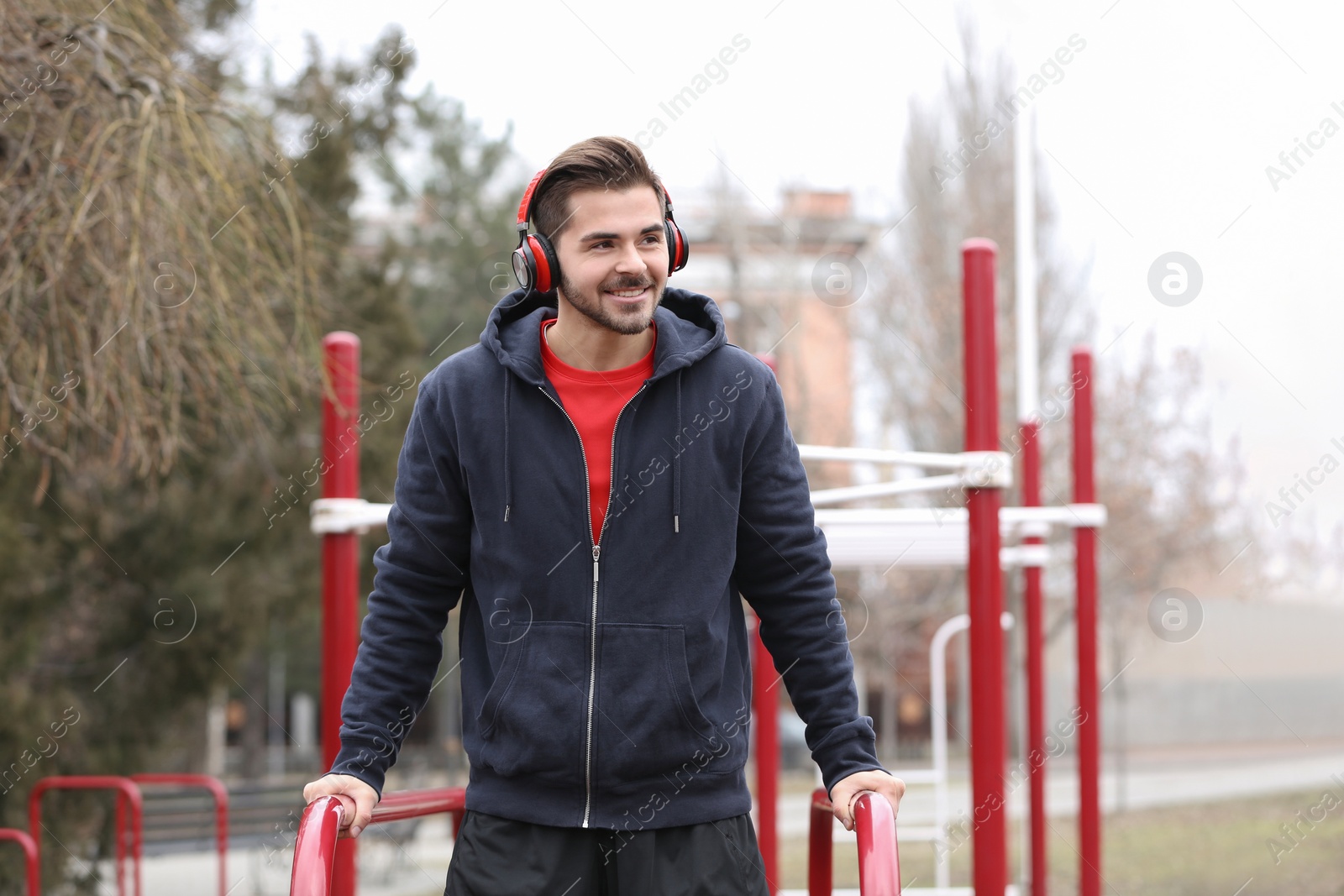 Photo of Young man with headphones listening to music and exercising on sports ground