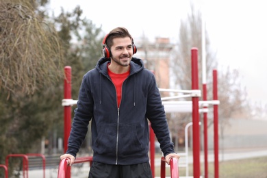 Young man with headphones listening to music and exercising on sports ground