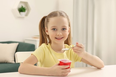 Cute little girl with tasty yogurt at white table at home
