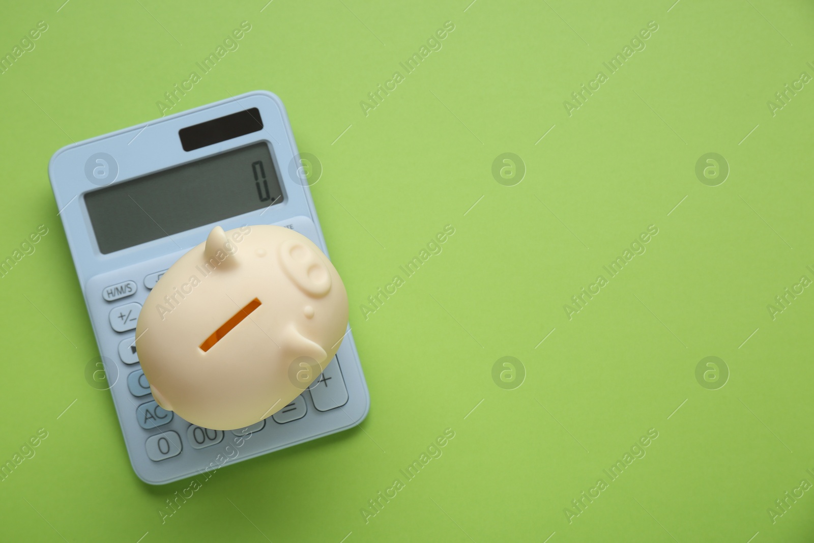 Photo of Piggy bank and calculator on light green background, top view. Space for text