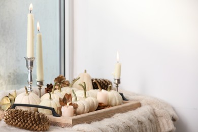 Photo of Tray with white pumpkins, burning candles, pine cones and dry leaves on window sill indoors. Space for text