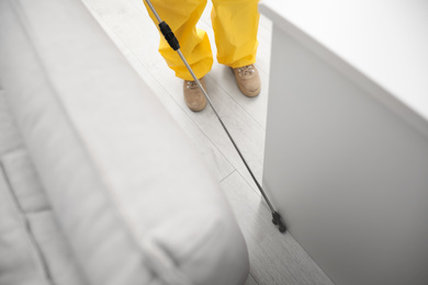 Photo of Pest control worker spraying pesticide around furniture indoors, above view
