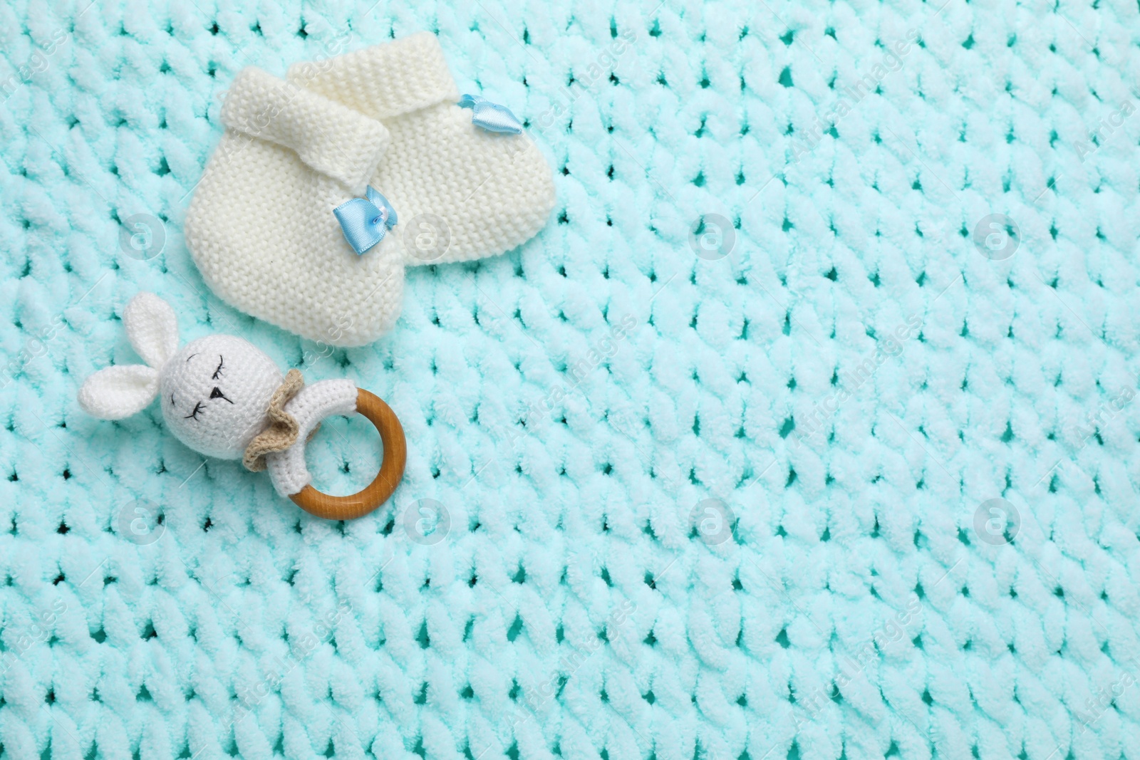 Photo of Cute baby booties and toy on light blue knitted fabric, flat lay. Space for text