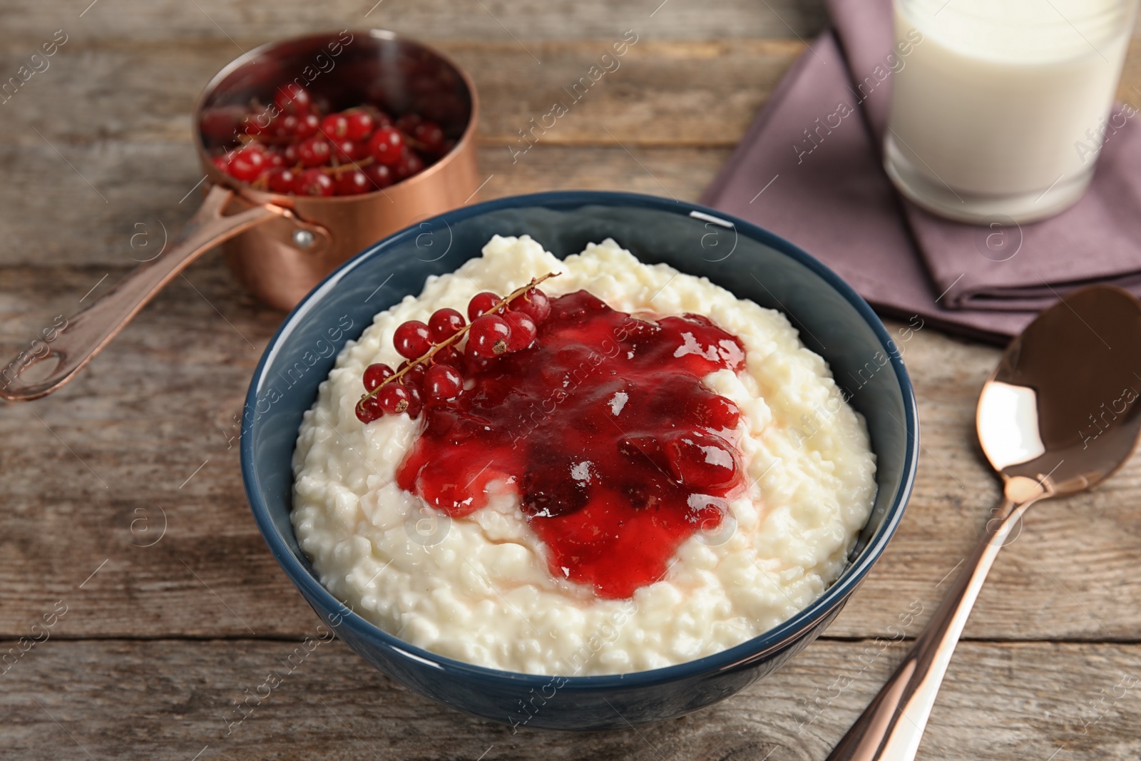 Photo of Creamy rice pudding with red currant and jam in bowl served on wooden table