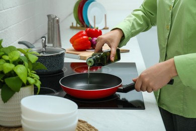 Photo of Woman pouring cooking oil from bottle into frying pan in kitchen, closeup