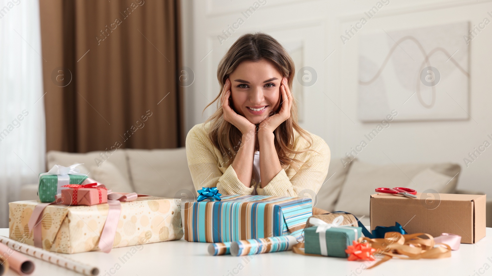 Photo of Young woman with beautifully wrapped gifts at table in living room