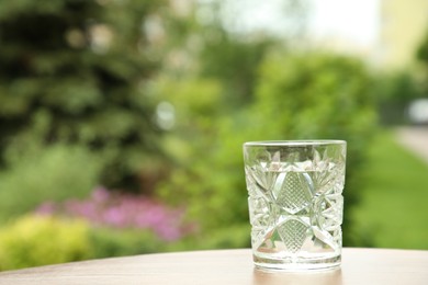 Glass of fresh water on wooden table outdoors, space for text