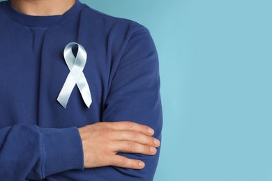 Closeup view of man with ribbon on light blue background, space for text. Urology cancer awareness