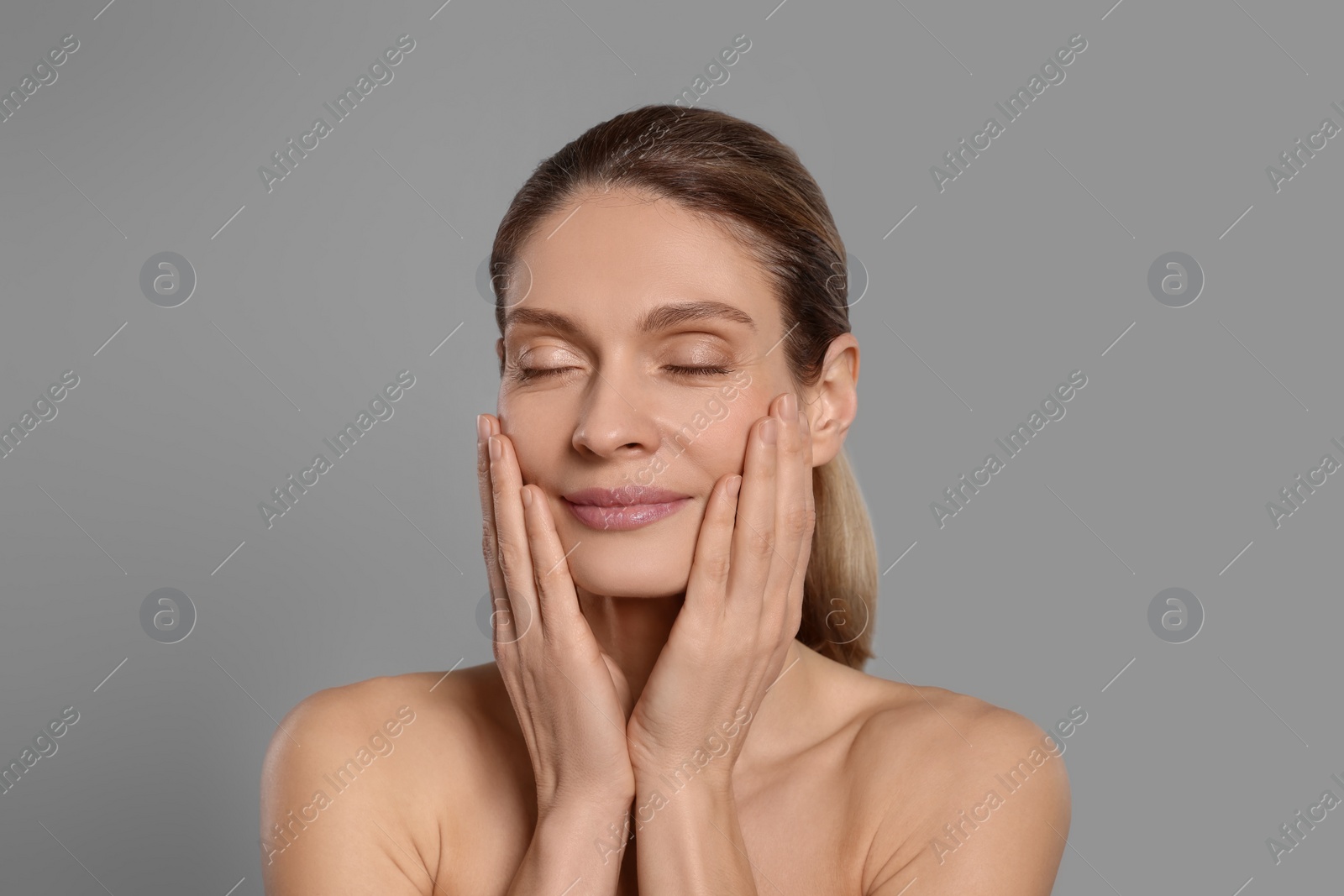 Photo of Woman massaging her face on grey background