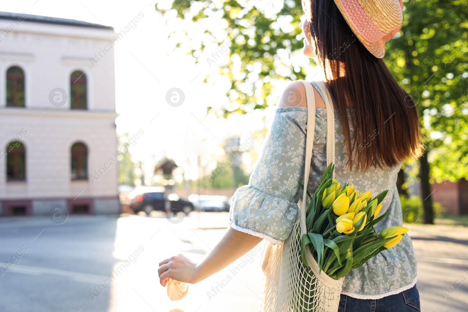 Photo of Young woman with bouquet of yellow tulips on city street, back view. Space for text