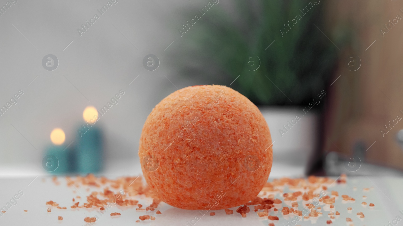 Photo of Orange bath bomb with salt on countertop near tub indoors, closeup. Bokeh effect