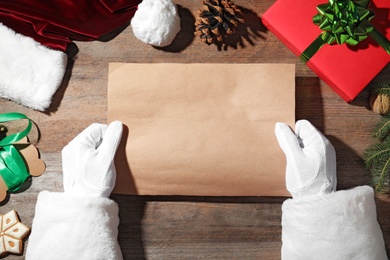 Santa Claus holding empty paper at wooden table, top view. Space for text