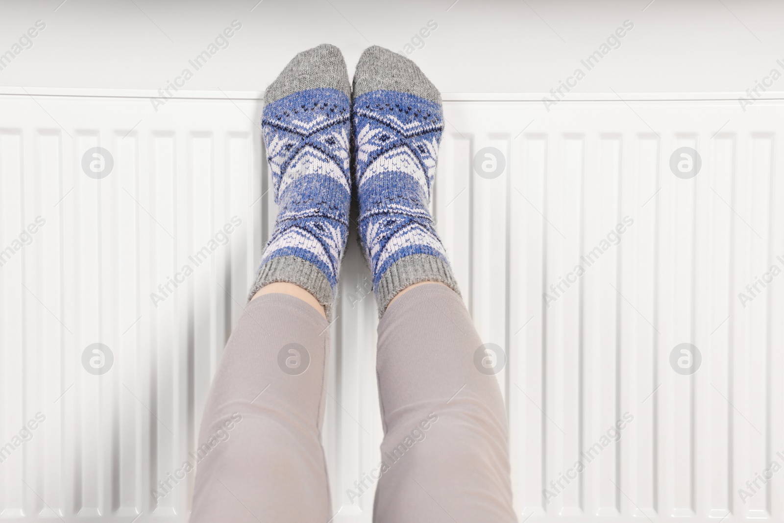 Photo of Woman warming feet near heating radiator, closeup