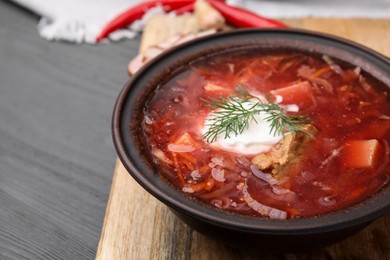 Tasty borscht with sour cream in bowl on grey wooden table, closeup. Space for text