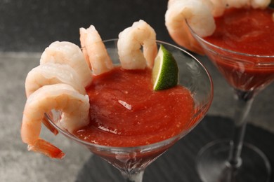Photo of Tasty shrimp cocktail with sauce and lime in glasses on grey table, closeup