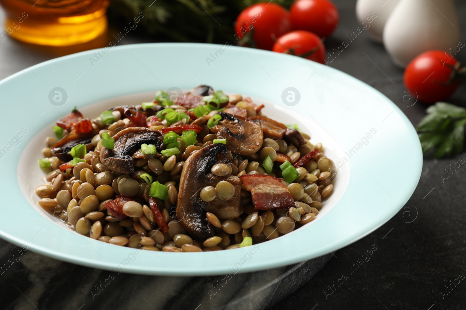 Photo of Delicious lentils with mushrooms, bacon and green onion on grey table, closeup