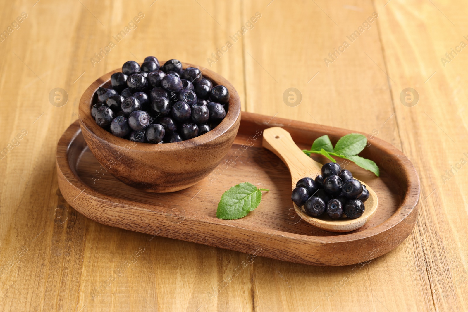 Photo of Bowl, spoon with tasty fresh bilberries and leaves on wooden table