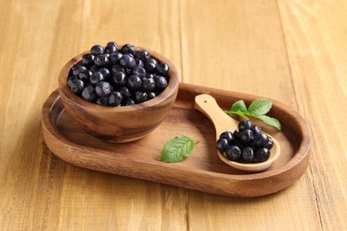 Bowl, spoon with tasty fresh bilberries and leaves on wooden table