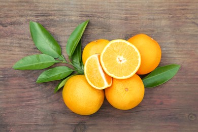 Many ripe oranges and green leaves on wooden table, flat lay