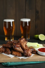 Photo of Delicious chicken wings served with beer on black wooden table