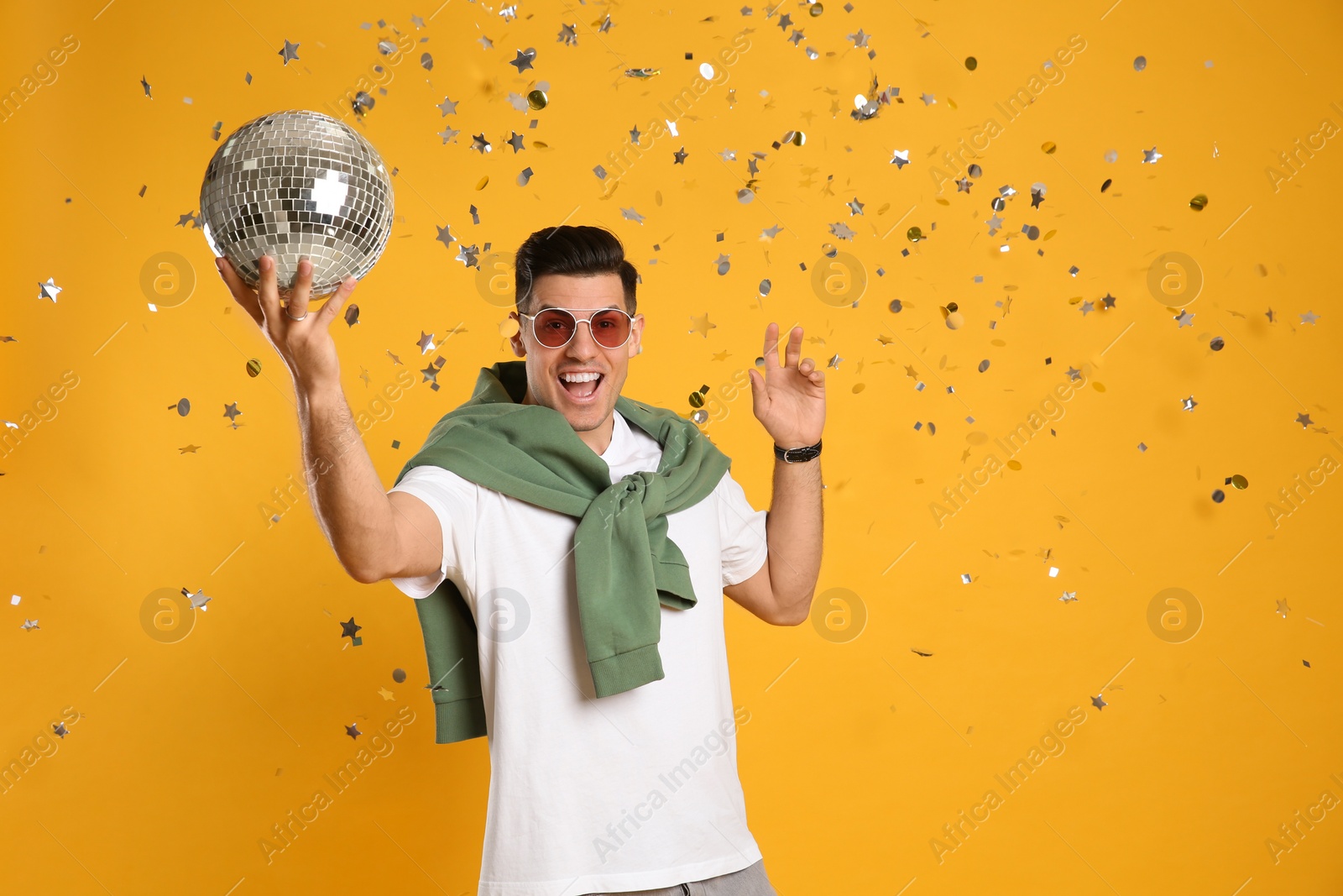 Photo of Happy man with disco ball and confetti on yellow background