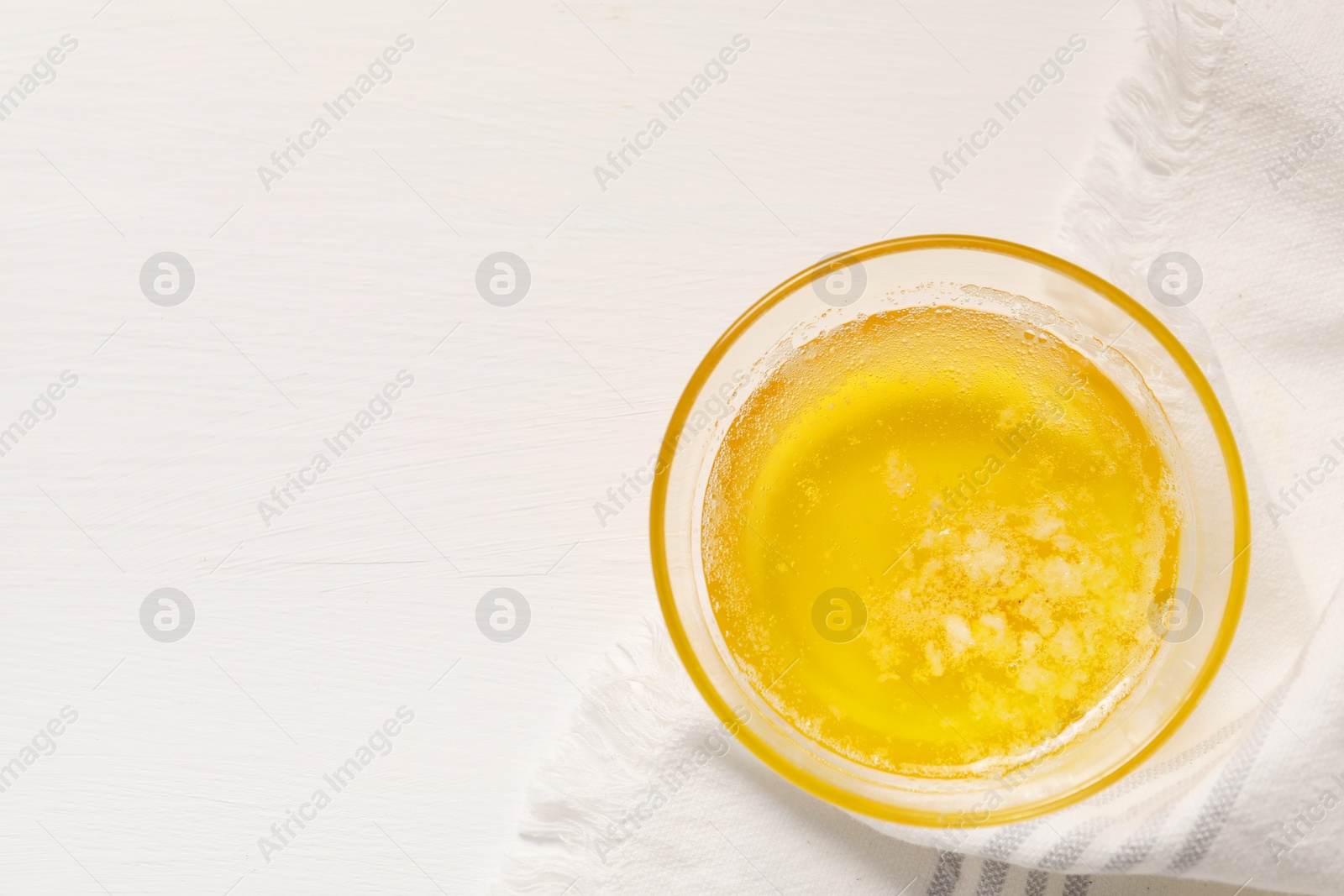 Photo of Melted butter in glass bowl on white wooden table, top view. Space for text