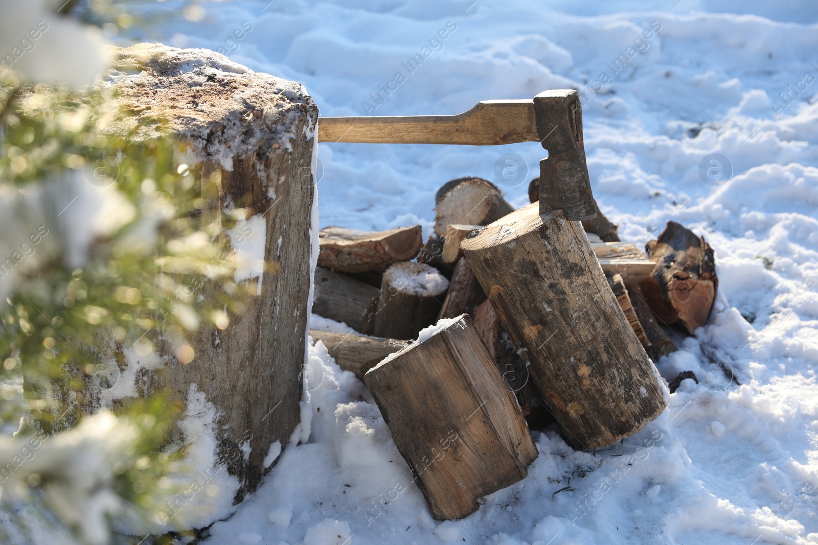 Photo of Metal axe in wooden log and pile of wood outdoors on sunny winter day