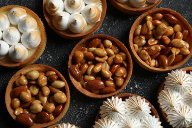 Many different tartlets on black textured table, flat lay. Tasty dessert