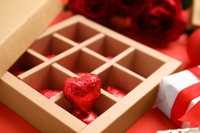 Photo of Tasty heart shaped chocolate candies in box on red background, closeup. Valentine's day celebration